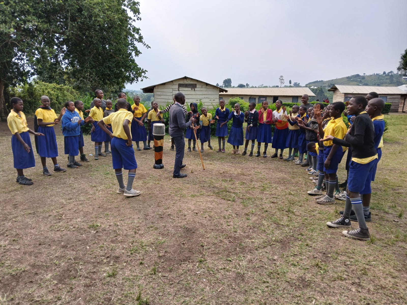 Pupils singing and drumming on the school field, with the timber classroom blocks behind